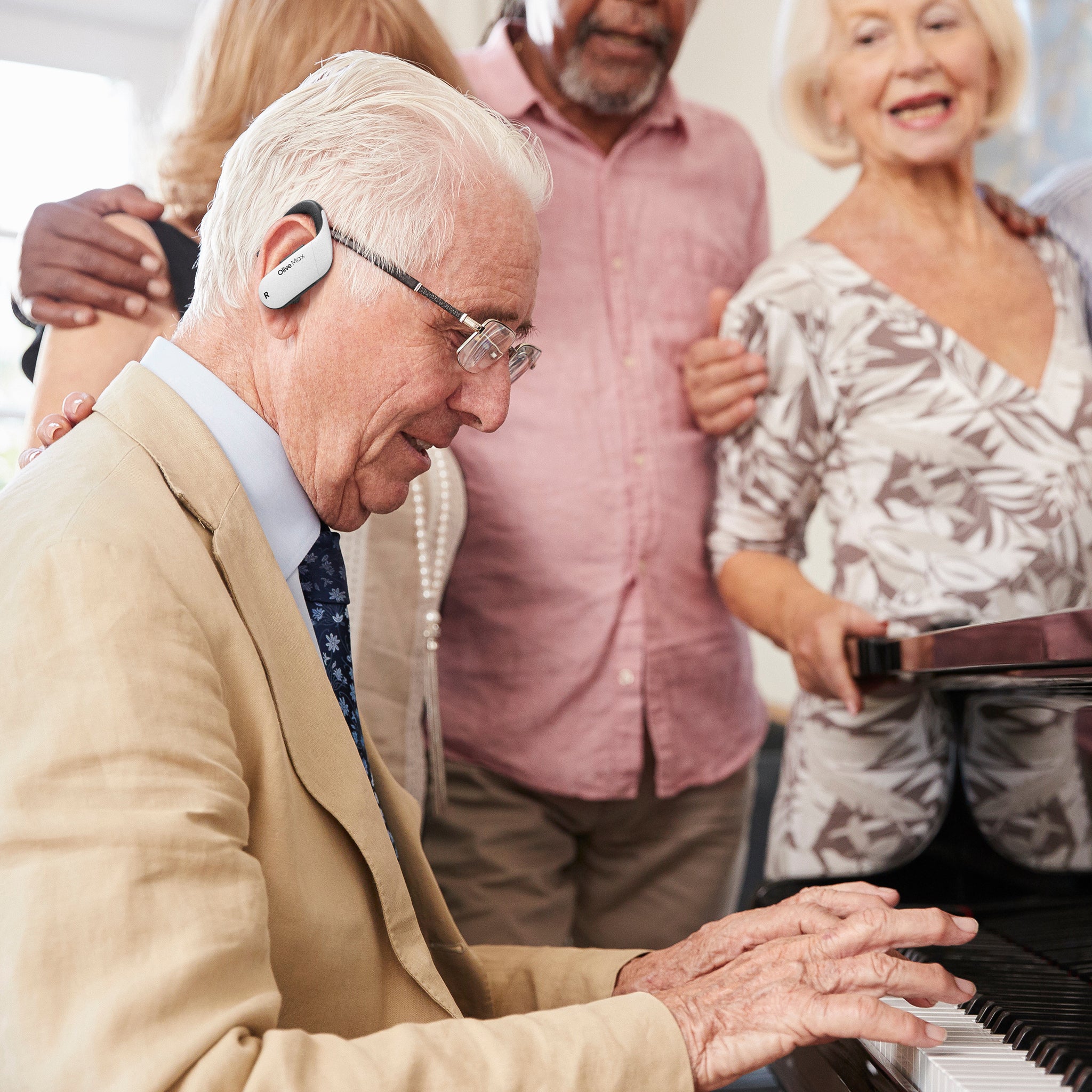 Elderly man with white hair playing the piano in front of friends, all benefiting from enhanced piano sounds and clearer voices thanks to Olivemax hearing aids.