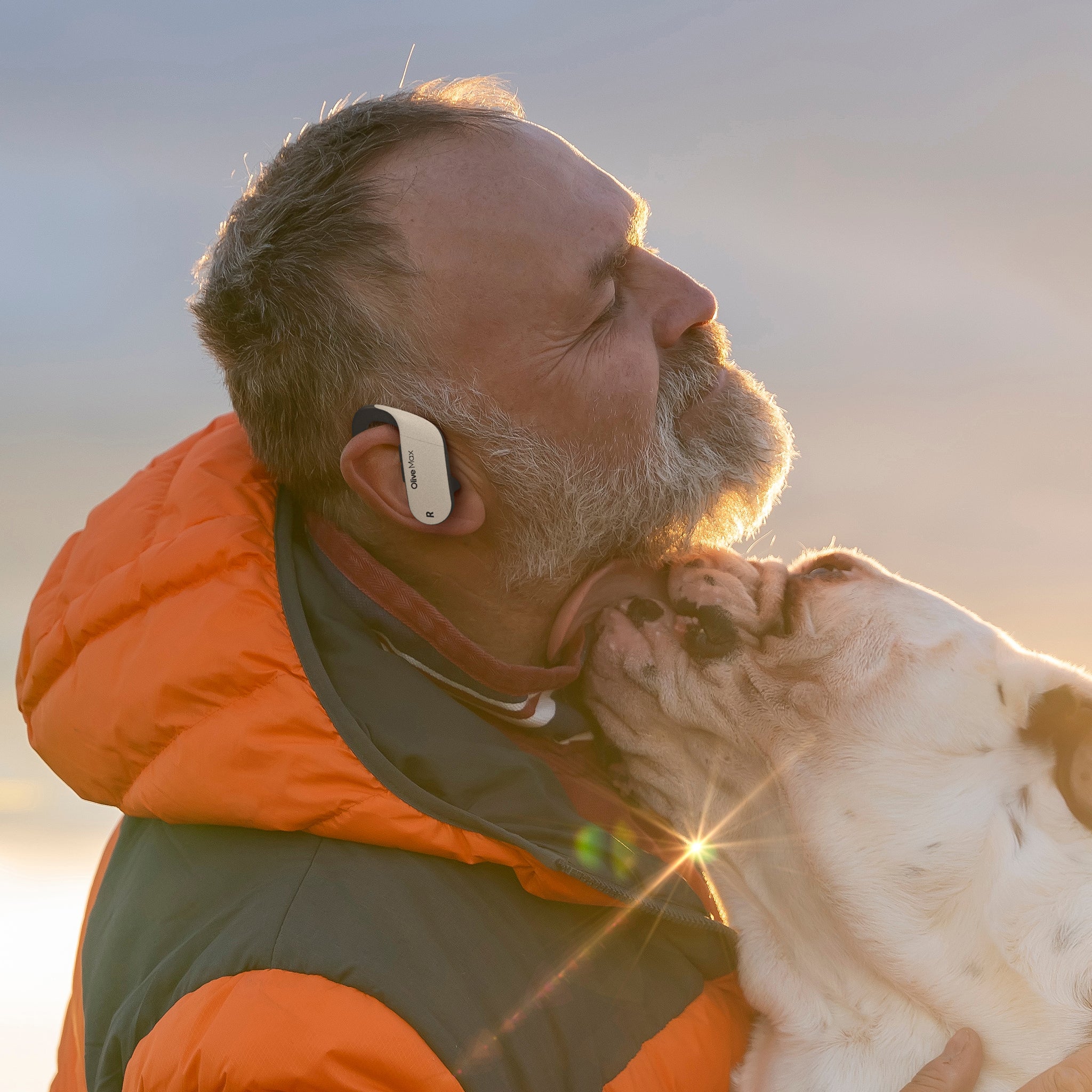 Joyful man with closed eyes receives a visit from his dog, savoring the moment and the sounds of the environment, enhanced by Olive Max hearing aids.